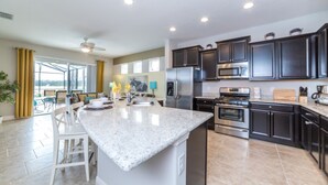 A modern kitchen with dark cabinets, stainless steel appliances, and a large island. - The Ultimate 5 Bedroom 4 Bathroom Solterra (Davenport)