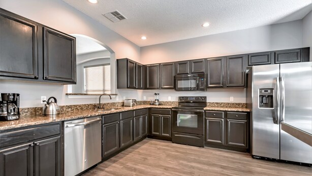 A modern kitchen with dark cabinets, stainless steel appliances, granite countertops, and a wood floor. - Oasis Key Villa Emerald Island (Kissimmee)