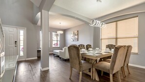 A dining area with a wooden table, beige upholstered chairs, and a modern pendant light. - Oasis Key Villa Emerald Island (Kissimmee)