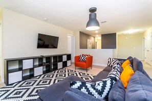 A modern living room with a sectional sofa, a red chair, a black and white patterned rug, and a TV mounted on the wall. - 1474rf Champions Gate 9 Bedroom 5 Bathroom Villa (Davenport)