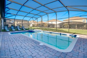 A covered swimming pool with a clear blue water feature, surrounded by a brick patio and a transparent roof structure. - 1474rf Champions Gate 9 Bedroom 5 Bathroom Villa (Davenport)