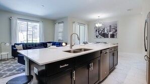 A modern kitchen with a large island, black cabinetry, and a blue sofa in the adjacent living area. - Stinger Drive Villa Champions Gate 2 (Davenport)