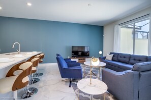 Uma sala de estar moderna com sofá, cadeiras, televisão e um espaço de refeições com pia e cadeiras.