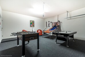 Une pièce avec une table de baby-foot, une table de ping-pong, un fauteuil rouge et un tableau coloré accroché au mur.