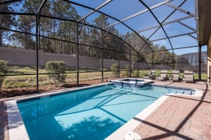 Una piscina exterior techada con vistas despejadas del paisaje circundante, que incluye árboles y un muro de ladrillo.