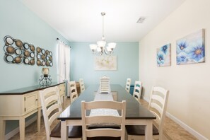 A dining room with a long table, white chairs, a chandelier, and wall art.