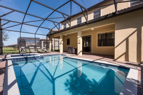 A swimming pool with a glass enclosure, adjacent to a building with a tiled patio and outdoor seating.