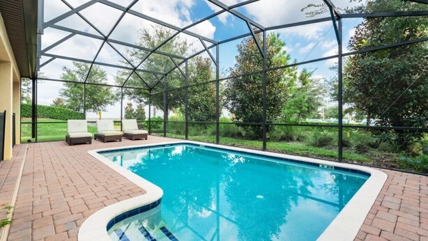 A swimming pool with a glass enclosure, surrounded by a brick patio and lounge chairs. - Showhome 5 Bedroom Champions Gate Villa 1401mvd (Davenport)