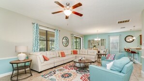 A living room with a beige sectional sofa, a teal armchair, a coffee table, and a patterned rug. - Showhome 5 Bedroom Champions Gate Villa 1401mvd (Davenport)