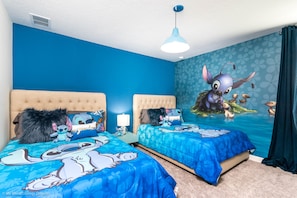 A bedroom with two beds, blue bedding, and a wall mural of Stitch from Lilo & Stitch.