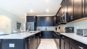 A modern kitchen with dark cabinetry, a central island, and stainless steel appliances.