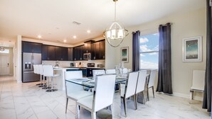 A modern kitchen with dark cabinets, stainless steel appliances, and a dining area with a glass table and white chairs.
