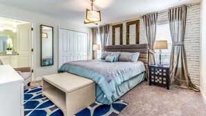 A bedroom with a bed, bedside tables, a bench, a mirror, and a window with curtains.