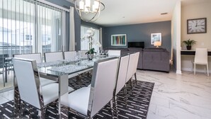 A modern dining area with a glass table, white chairs, and a chandelier. - 1565tl Champions Gate Furnished 6 Bedroom (Davenport)