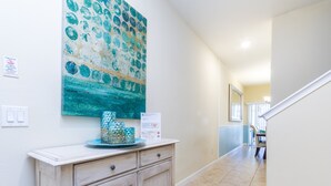 A hallway with a decorative wall piece, a wooden cabinet, and a dining area in the background.