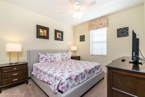 Quarto com cama, mesas de cabeceira, escrivaninha, ventilador de teto e decorações nas paredes.