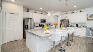 A modern kitchen with white cabinets, stainless steel appliances, a granite countertop, and a central island with bar stools. - 6121bod 11 Bedroom 9 Bathroom (Davenport)