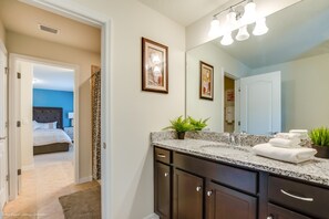 A bathroom with a granite countertop, dark cabinetry, a large mirror, and a potted plant. - 8875 Ultimate 8 Bedroom 6 Bathroom Windsor (Kissimmee)