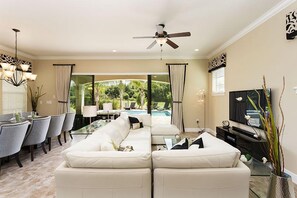 A modern living room with a sofa set, a dining area with chairs, a TV, and a ceiling fan.