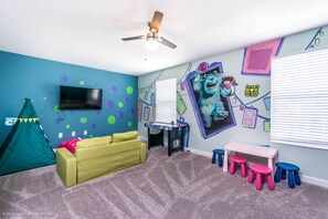 A child's room with a blue wall, a green couch, a pink table, and a ceiling fan.