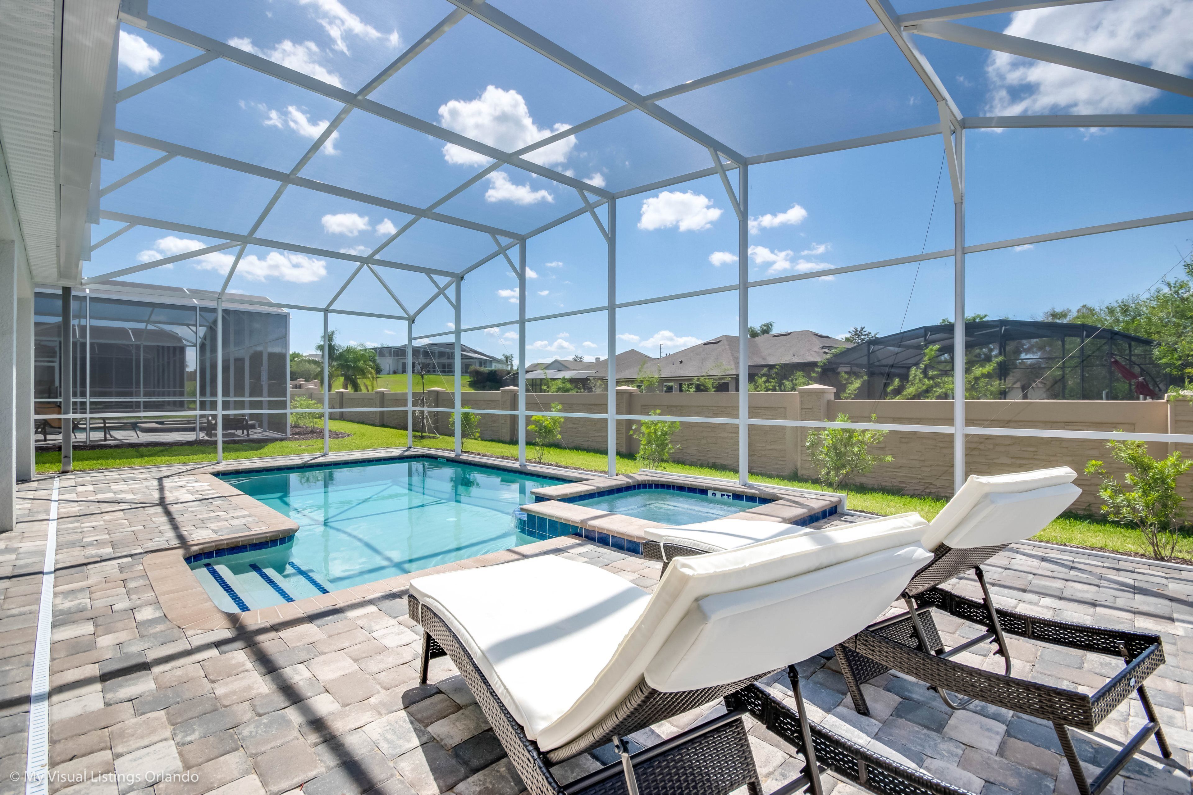 A covered outdoor swimming pool with lounge chairs and a hot tub.