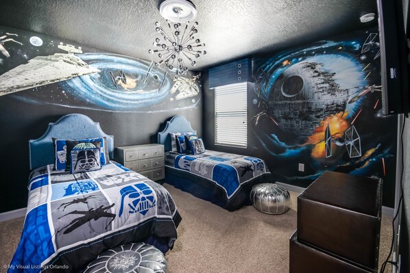 Une chambre avec deux lits, un ventilateur de plafond et une fresque murale représentant des œuvres d’art sur le thème de l’espace.