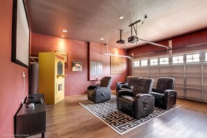 A home theater room with a brick wall, a ticket booth, leather recliners, a projector, and a garage door.