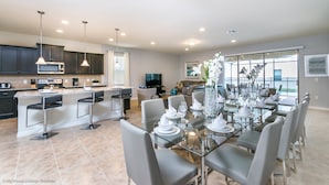 A modern kitchen with dark cabinets, a central island, and a dining area with a glass table and chairs. - 1852nc 8 Bedroom 6 Bathroom Windsor (Kissimmee)