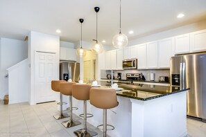 A modern kitchen with white cabinets, stainless steel appliances, and a central island with bar stools.