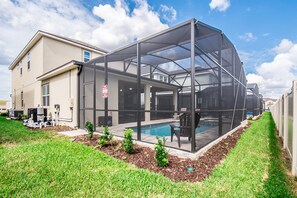 A house with a covered outdoor swimming pool, a lawn, and a small garden area. - Amazing 6 Bedroom 5 Bathroom Solara Resort Villa (Kissimmee)