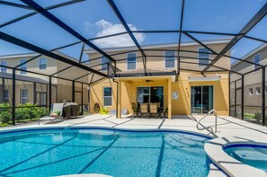 An indoor swimming pool with a glass enclosure, a patio area with outdoor furniture, and a building with multiple windows in the background. - Ultimate 6 Bedroom 5 Bathroom Solterra Resort Home (Davenport)