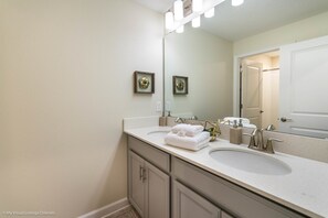A bathroom with two sinks, a large mirror, and a door leading to a shower. - Windermere Villa Storey Lake (Kissimmee)