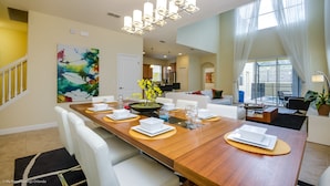 Un espace repas moderne avec une table en bois pouvant accueillir six personnes, des chaises blanches et un lustre contemporain.