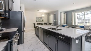 Una cocina moderna con armarios oscuros, una isla grande con un lavamanos y una zona de comedor con candelabro.