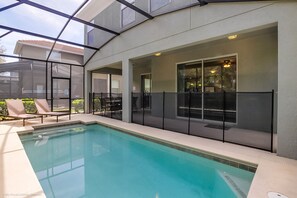 A swimming pool with a glass enclosure, outdoor seating, and a view of the surrounding area. - Cuban Place 8949 Paradise Plams (Kissimmee)
