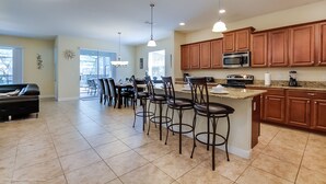 A spacious kitchen with a central island, bar stools, wooden cabinets, and a microwave.