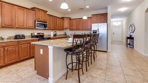 A spacious kitchen with wooden cabinets, a granite countertop, a central island with bar stools, and modern appliances.