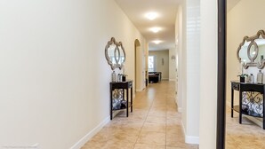 A hallway with a mirrored wall, a black console table with decorative items, and a light fixture on the ceiling.