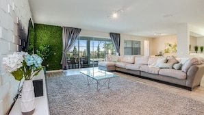 A modern living room with a sectional sofa, a glass coffee table, and a green wall.