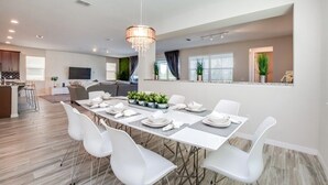 A modern dining area with a long table set for four, surrounded by white chairs.