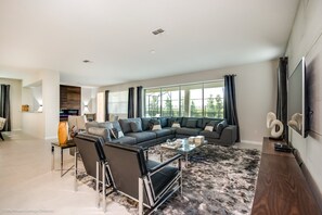 A modern living room with a sectional sofa, a glass coffee table, and a large window with curtains. - Solara Resort 9BD / 6BA Resort Villa 9043srl (Kissimmee)