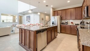 Une cuisine spacieuse dotée d’un îlot central, d’appareils électroménagers en acier inoxydable, de meubles en bois et de luminaires suspendus.