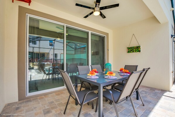 Un coin repas avec une porte vitrée donnant sur un patio, un ventilateur de plafond et un élément décoratif suspendu.