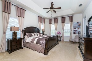 A bedroom with a large bed, a nightstand, a dresser, a chair, and a ceiling fan. - Castle Pines 1080 Reunion (Kissimmee)