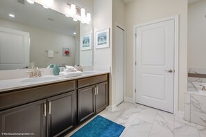 A modern bathroom with a large mirror, white vanity, dark cabinets, and a blue rug.