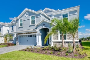 A two-story house with a stone facade, a garage, and a well-maintained lawn with young trees.