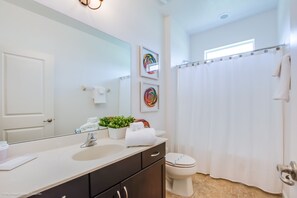 Ein modernes Badezimmer mit großem Spiegel, Waschbecken, Toilette und Duschvorhang.