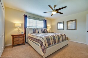 A bedroom with a bed, nightstands, a ceiling fan, and a window with curtains.
