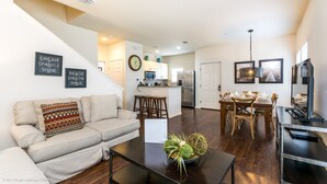 A modern living room with a sofa, coffee table, and a dining area with chairs and a table. - Lucaya Village Resort 4 Bedroom Townhome 2901 (Lake Buena Vista)