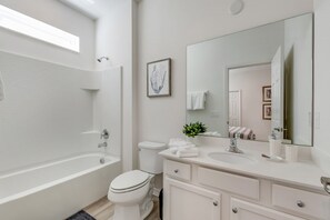Un baño moderno con bañera, inodoro y tocador con un espejo grande.